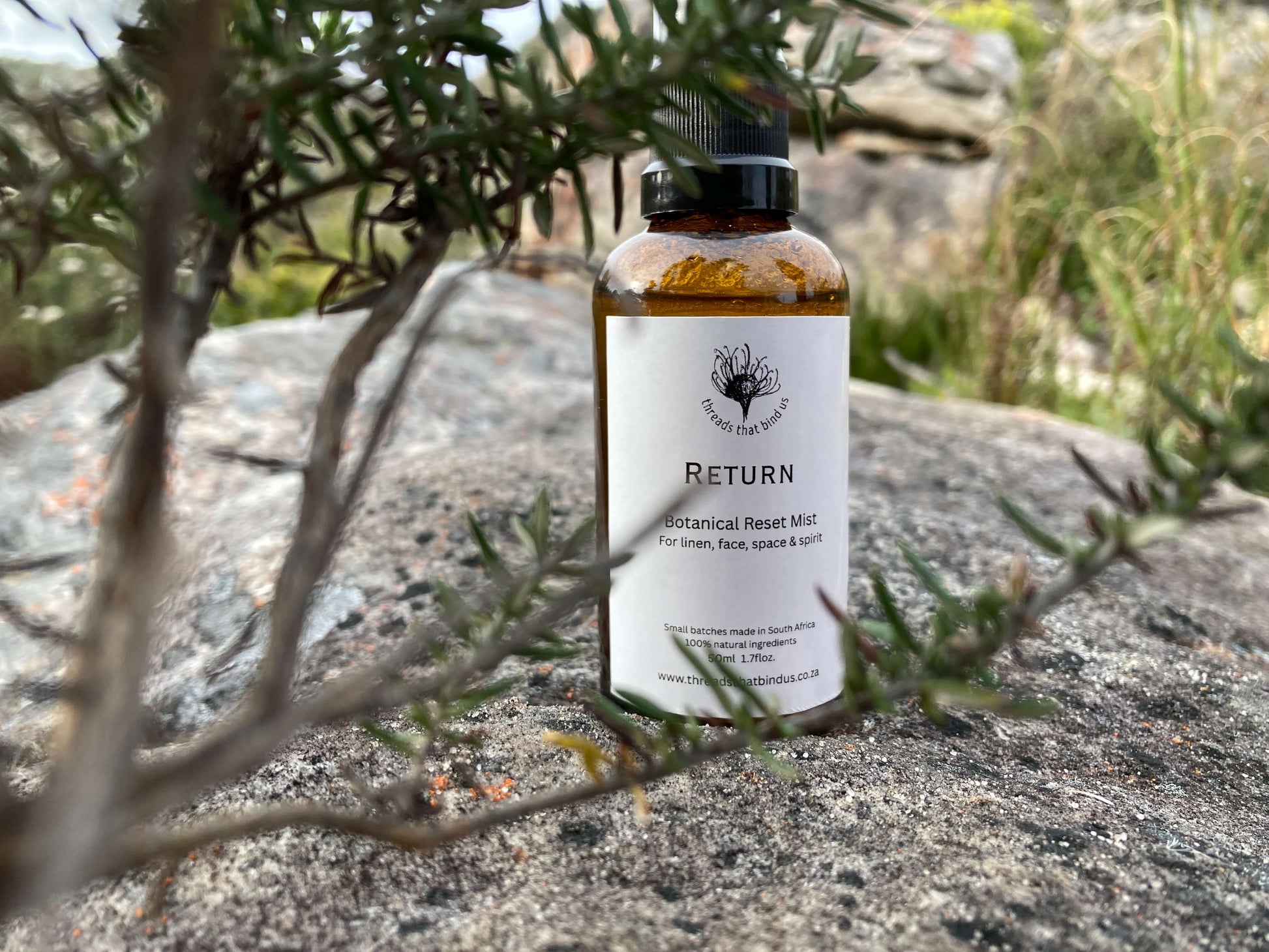 Bottle of 'Return' botanical reset mist on a rock with plants in the background